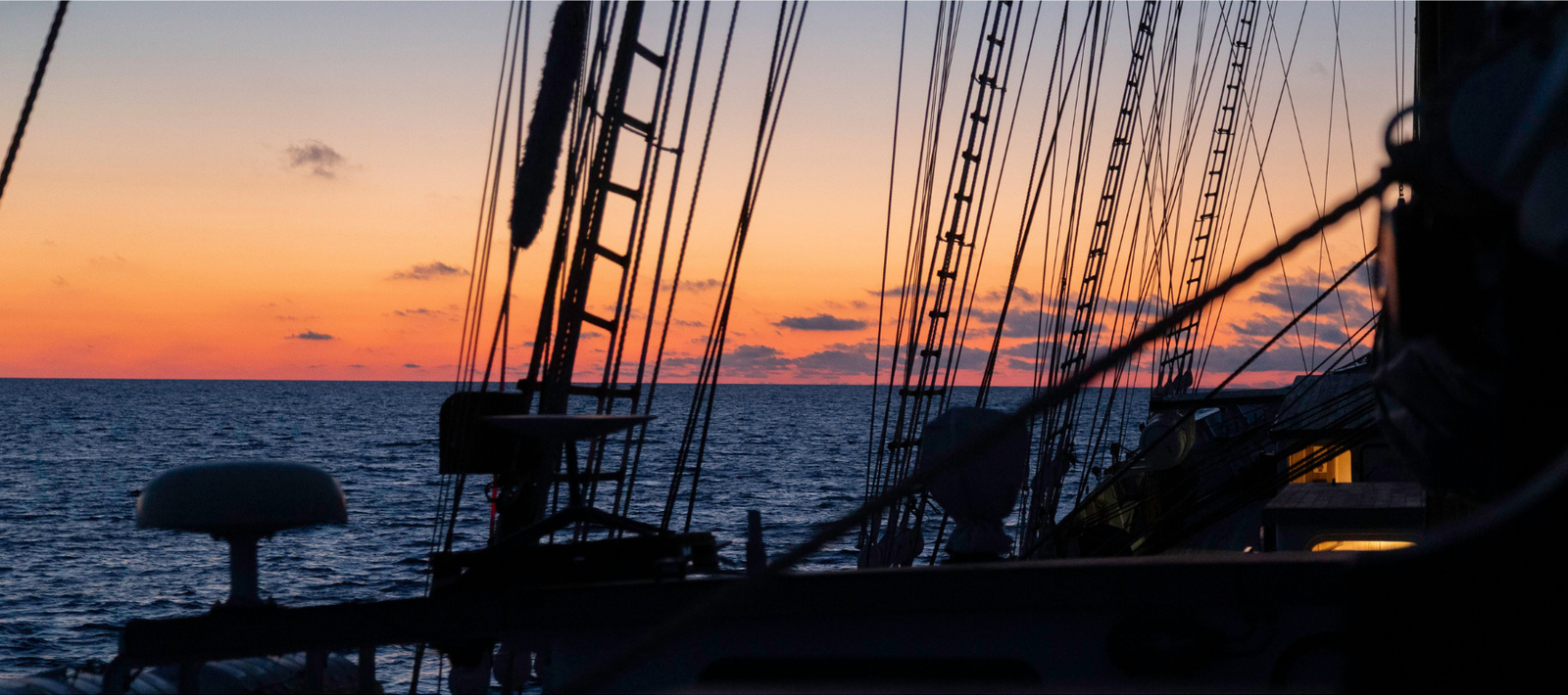 Silhouette of a tall ship against a sunset sky over the ocean