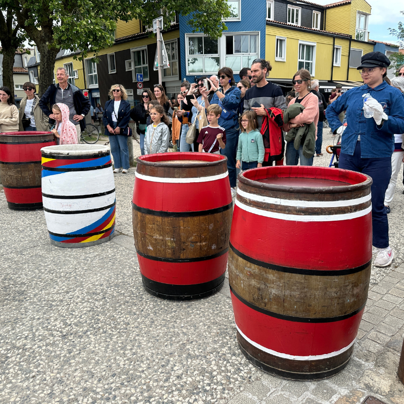 Decorative barrels with a colorful design on a street with people in the background.