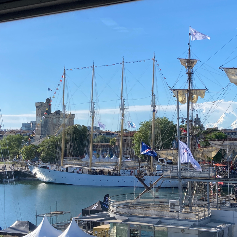 Historical ship docked at a harbor with a castle-like structure in the background.